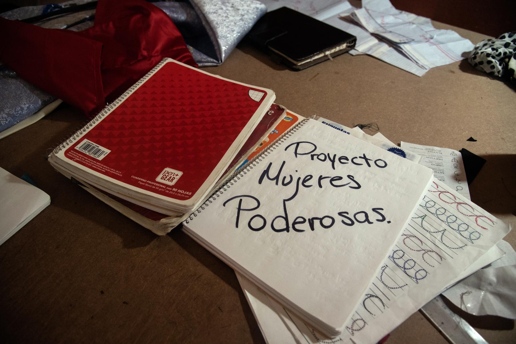 Varias libretas sobre un escritorio. Una de ellas se encuentra abierta y dice: "Proyecto Mujeres Poderosas".